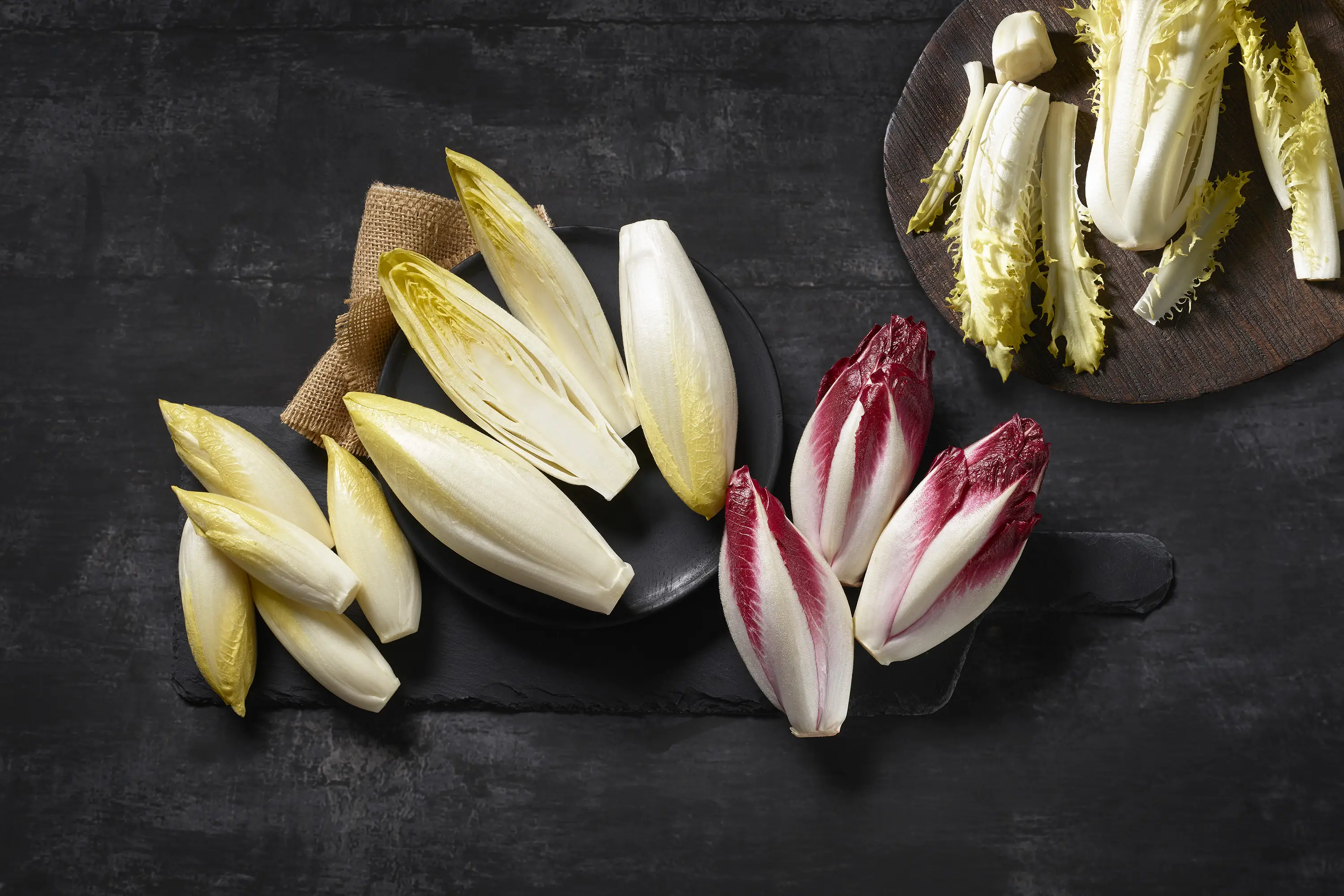 4 fajta cikória: fehér, piros, cikória, mini cikória és cikória, fadeszkán elrendezve.