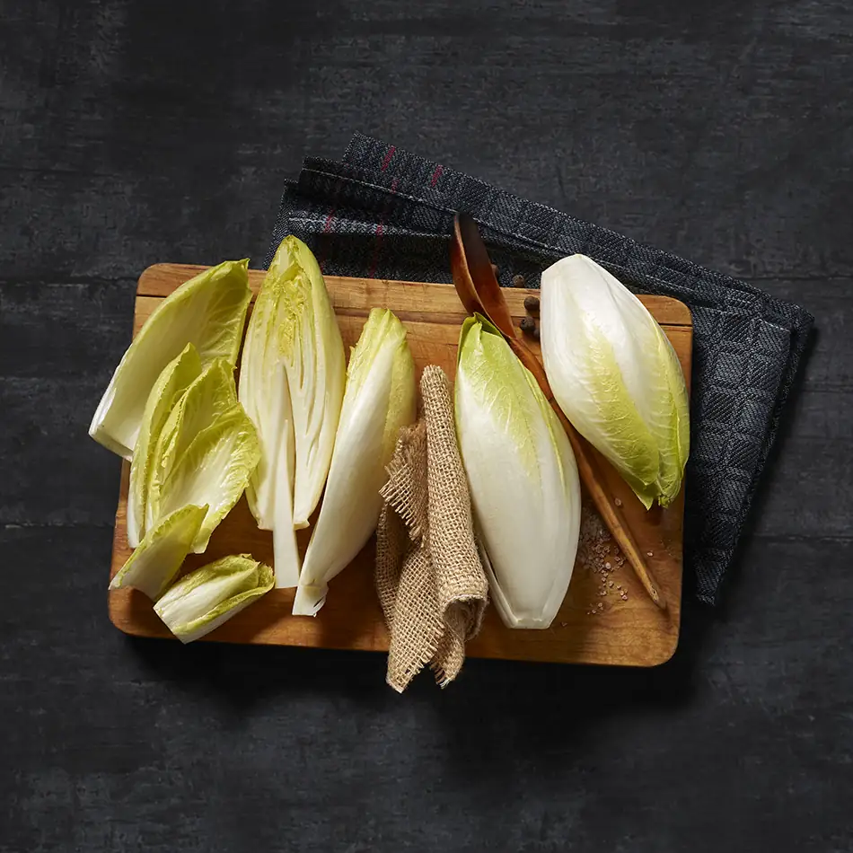 Több darab fehér cikória fadeszkán, részben félbevágva és a szárát kivágva.