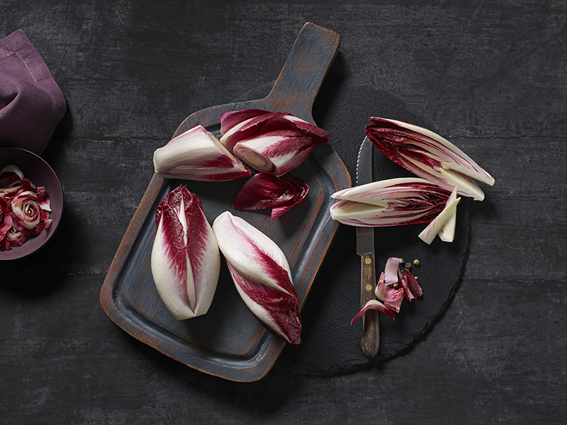 Több darab piros cikória egy fatáblán. Részben felvágva, a szárat eltávolítva