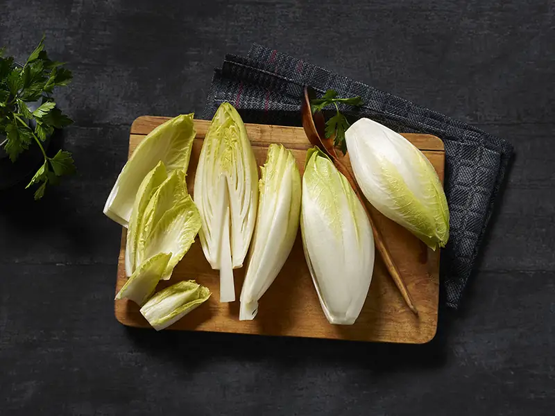 Több darab fehér cikória fadeszkán, részben félbevágva és a szárát kivágva.