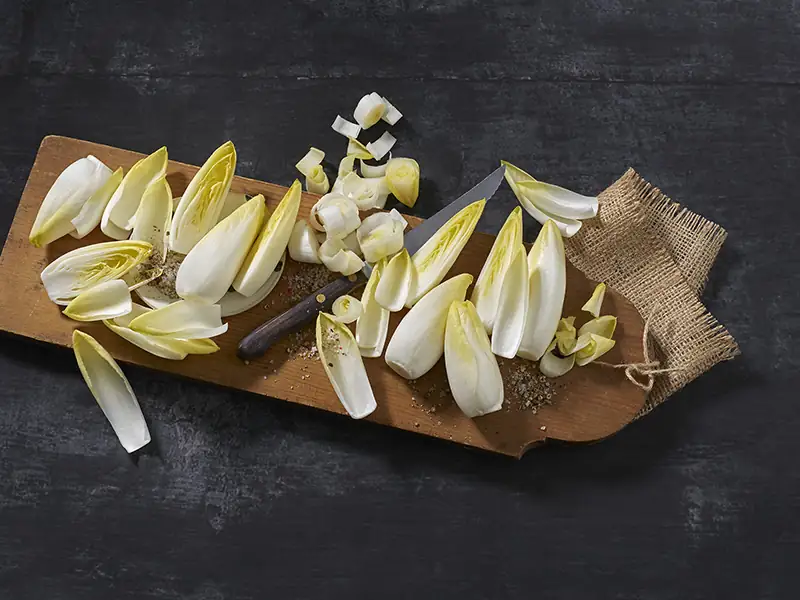 Cikória Mini cikória - több darab, részben felszeletelve, hosszúkás fadeszkán.